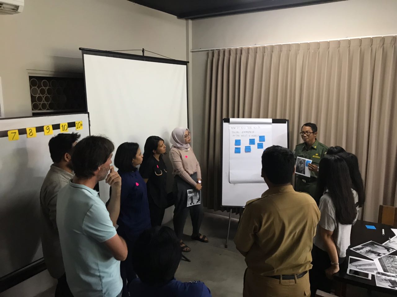 foto-peserta-berdiskusi-dengan-posisi-berdiri-mengelilingi-fasilitator-di-depan-flipchart-pada-kegiatan-pemetaan-profil-usaha-sosial-di-indonesia